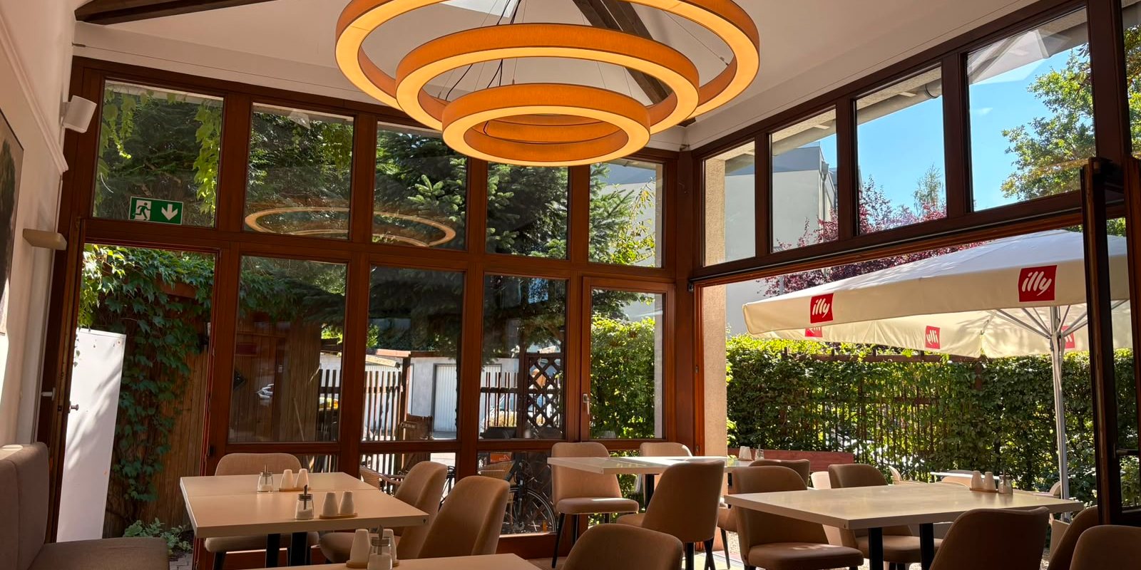 Wintergarten des Café Ava mit mehreren eingedeckten Tischen und Blick auf die Terrasse
